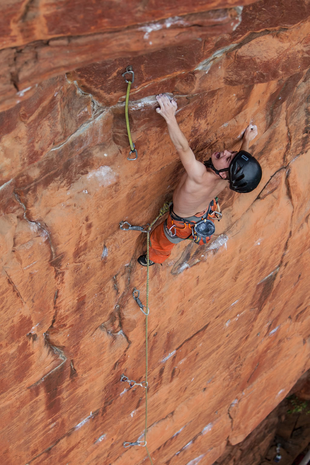 climber Mel Janse van Rensburg seen from above wears a helmet and screams while gripping a vertical rock wall